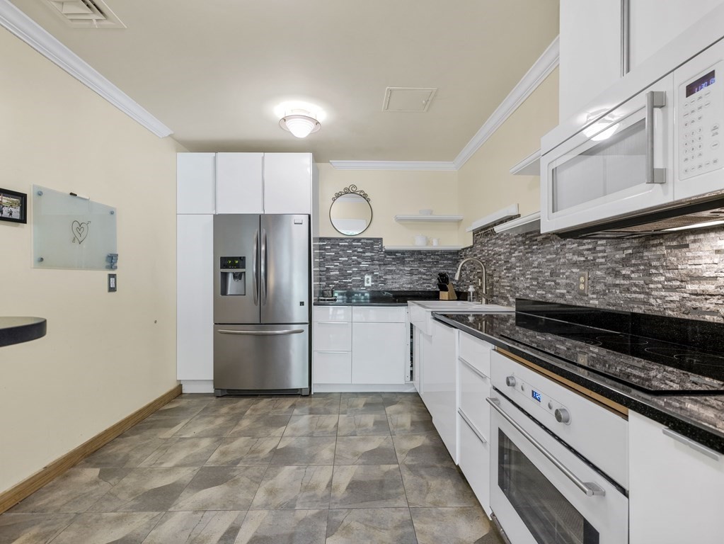 Kitchen with white cabinets, stainless steel appliances, and a gray stone-tile backsplash.