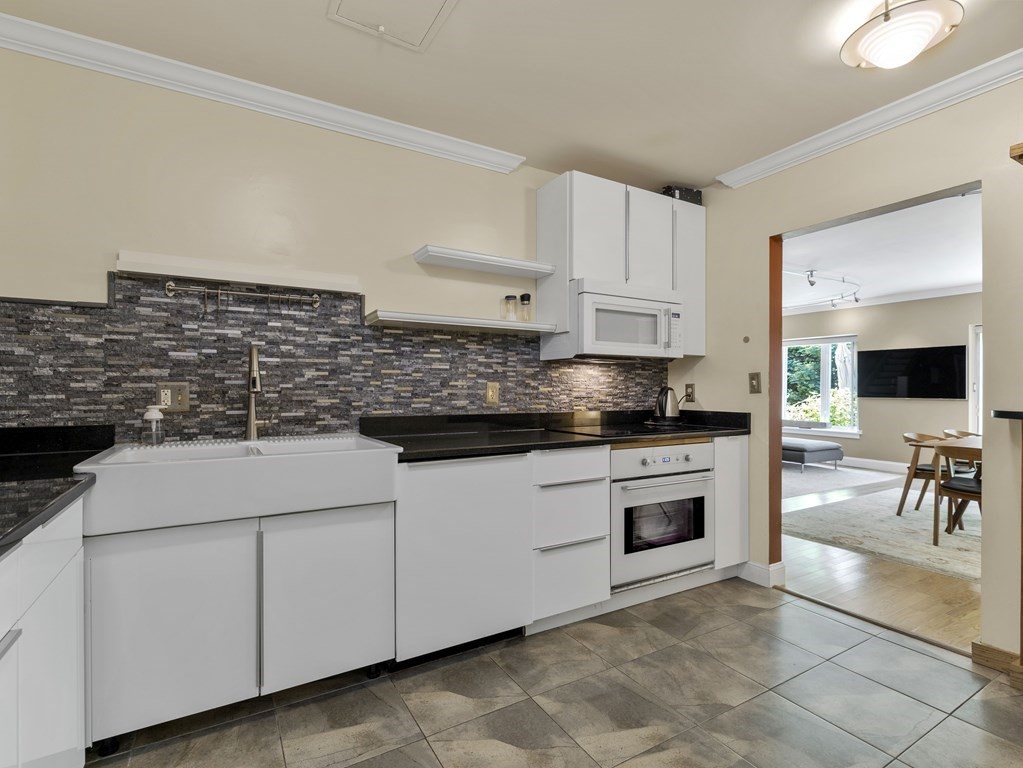 Kitchen with white cabinets, black countertops, farmhouse sink, and dark mosaic backsplash.