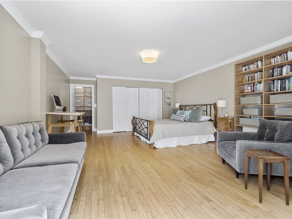 Bedroom with a central bed, gray sofas, hardwood floors, and full-height built-in bookshelves.