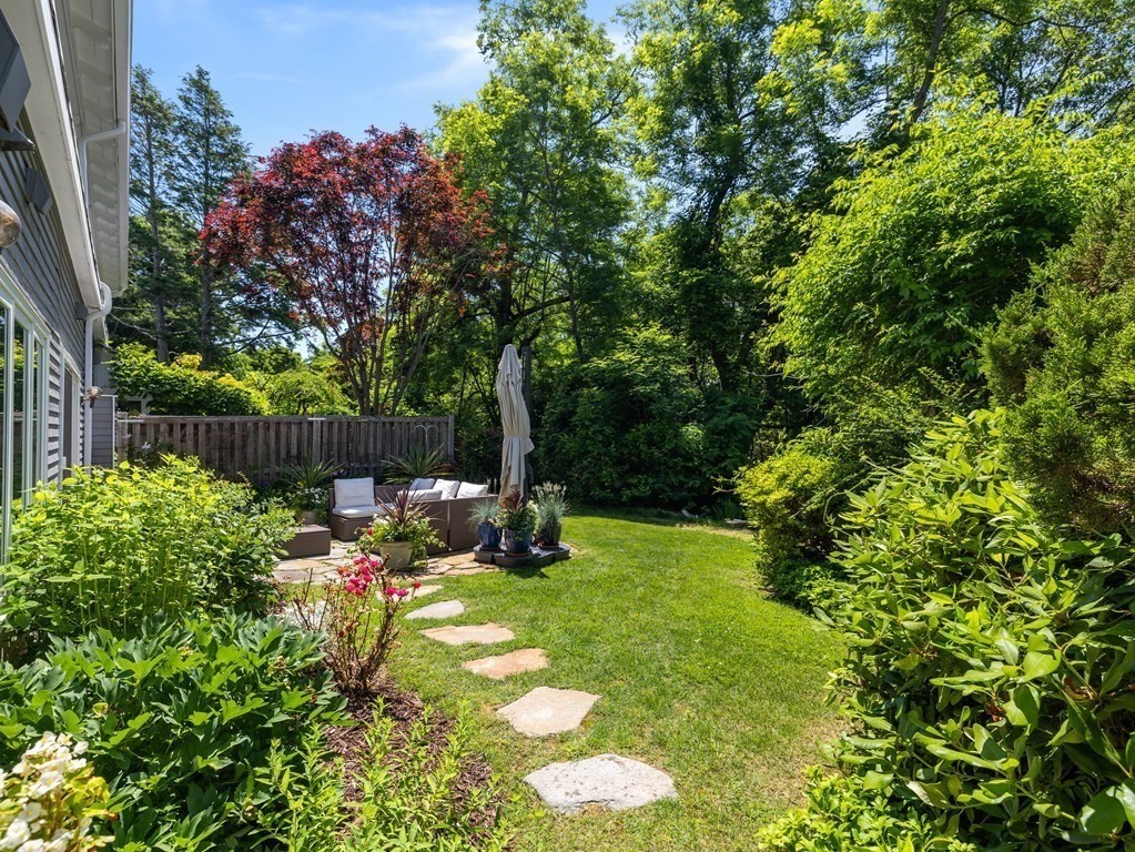 Landscaped backyard with a stepping-stone path leading to a furnished patio beneath mature trees.
