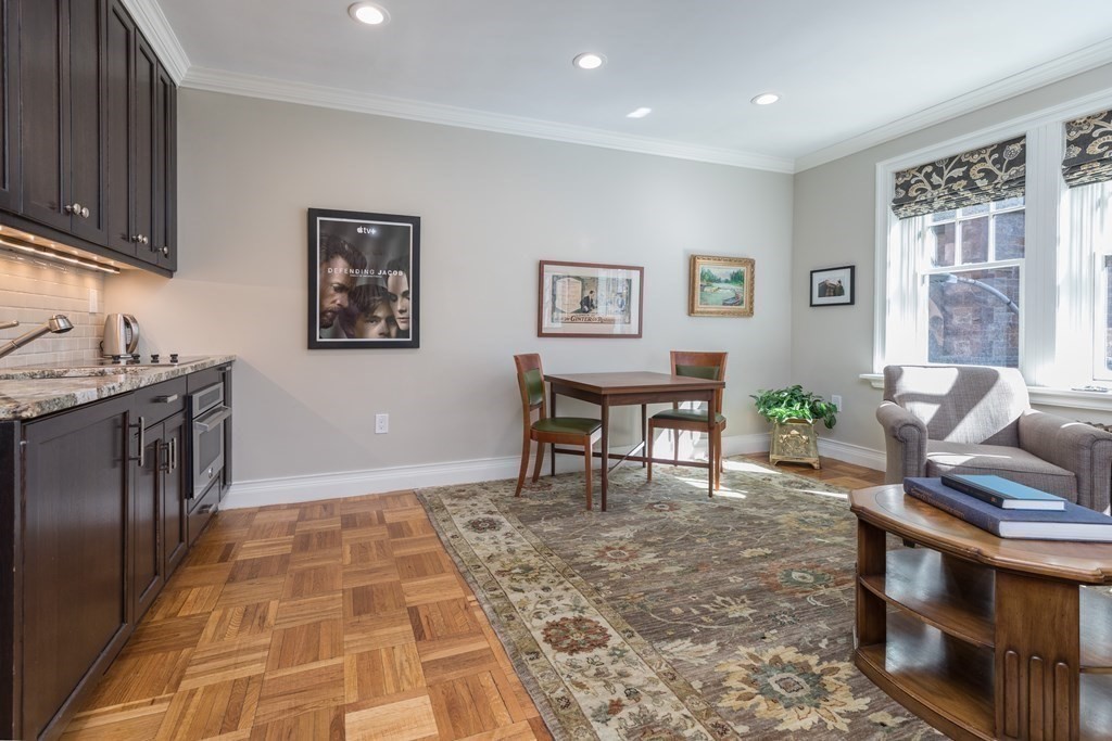 Living and dining area with dark wood kitchen cabinets, parquet flooring, and sunlit windows.
