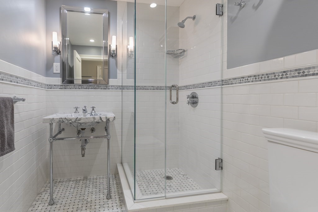 Bathroom with a glass-enclosed tiled shower and marble-topped pedestal sink.
