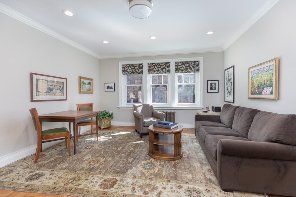 Living room with a gray sofa, dining table, and three sunlit windows.