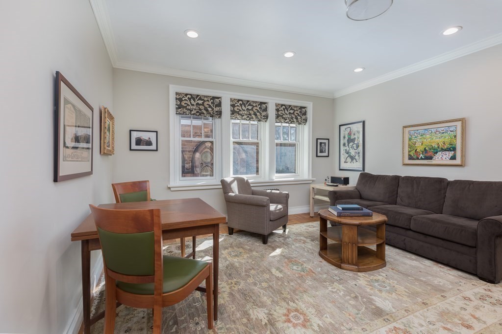 Living room with a dark gray sofa, wooden dining set, patterned rug, and three tall windows.
