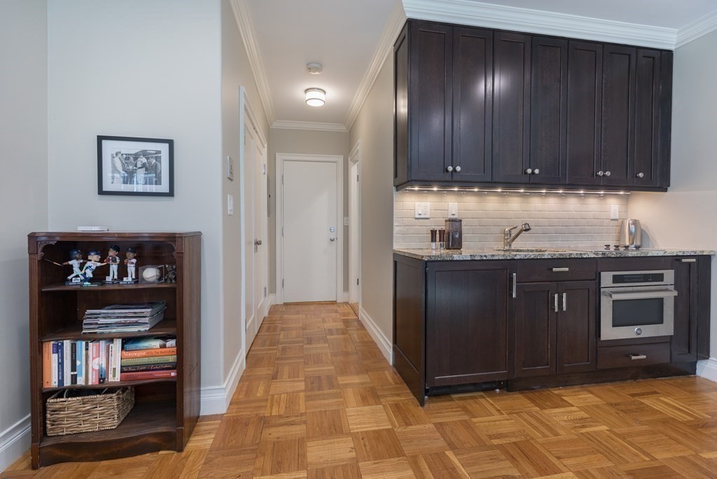 Kitchen with dark wood cabinets, stainless steel oven, and parquet floor beside a hallway.