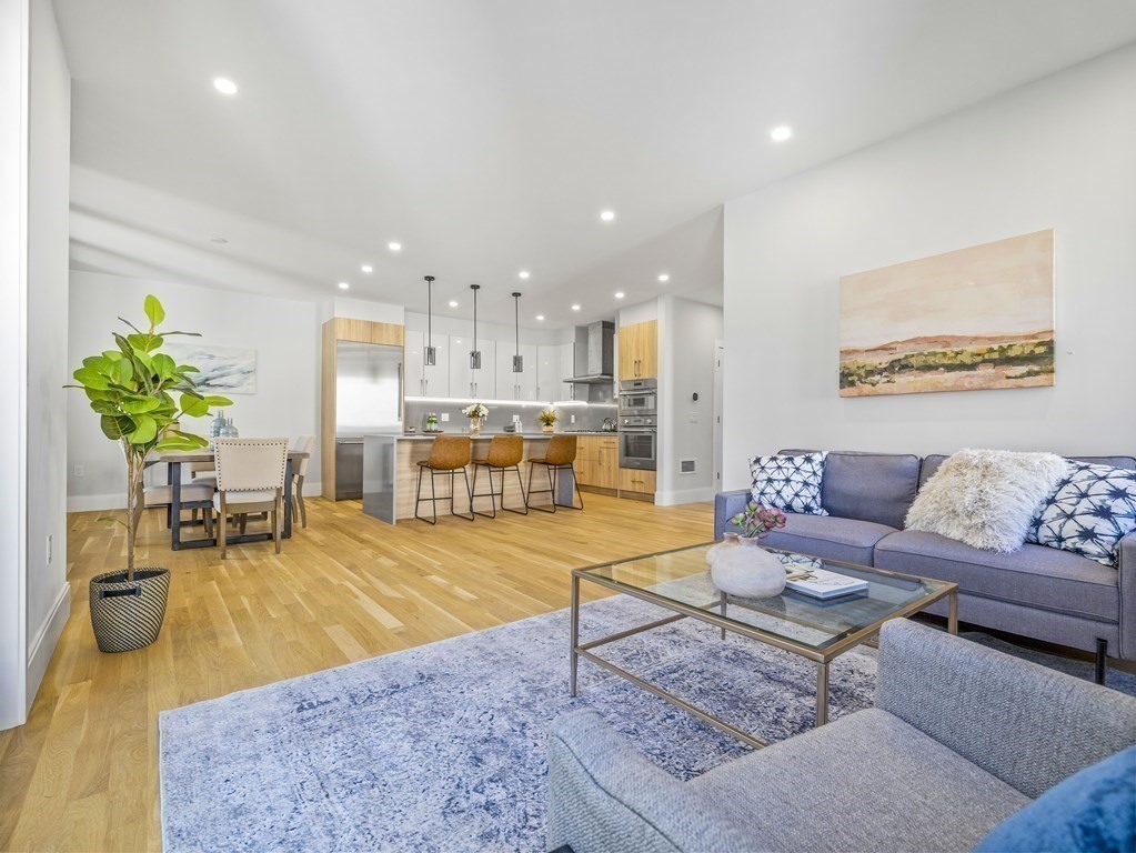 Open-plan living room and kitchen with light wood floors, white cabinetry, and a gray sofa.