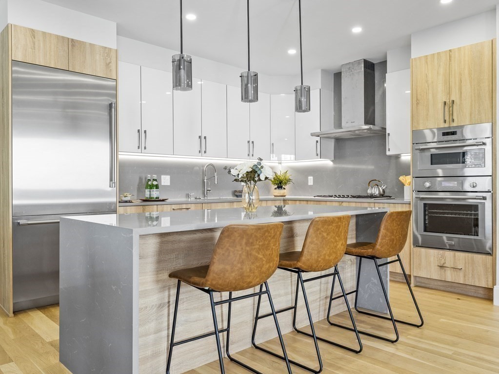 Modern kitchen with a large island, three brown bar stools, and stainless steel appliances.