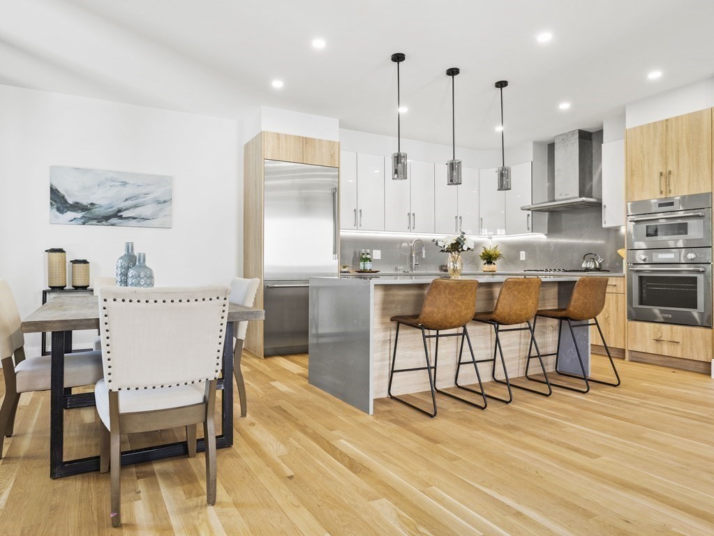 Open-plan kitchen and dining area with a large island, three bar stools, and light hardwood floors.