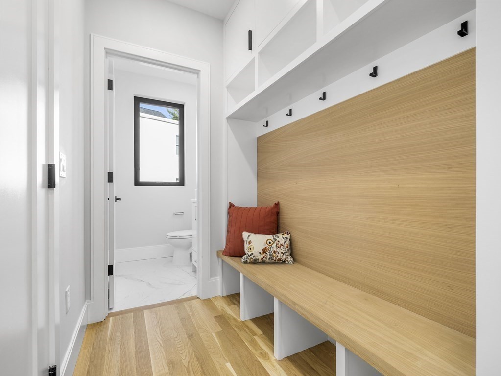 Mudroom with a long light wood built-in bench, black hooks, and overhead cubbies beside a bathroom doorway.