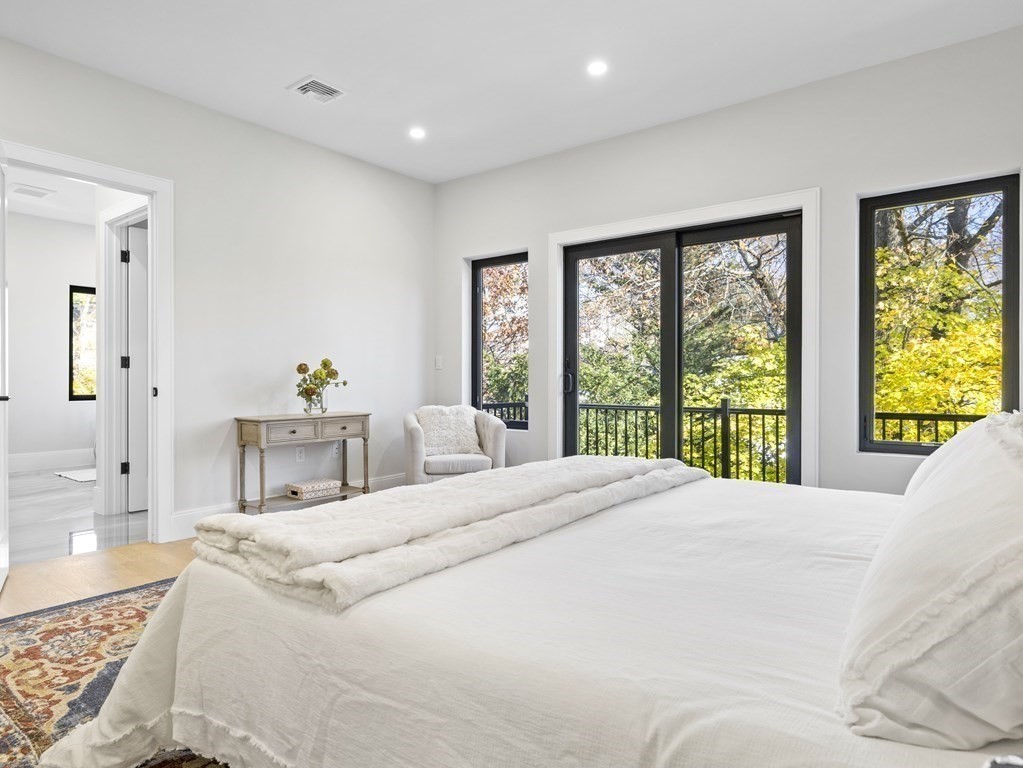 Bright bedroom with a white bed and black-framed windows overlooking leafy trees.