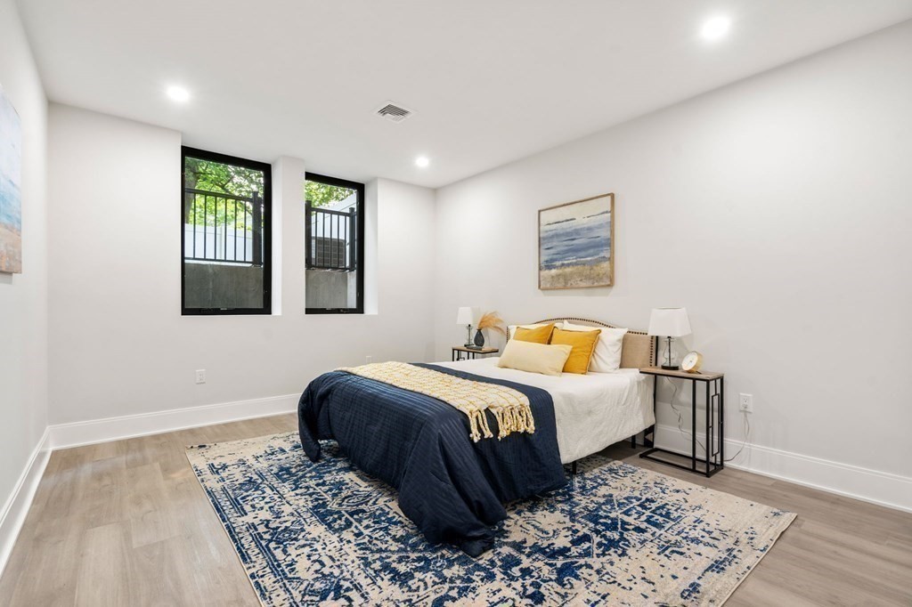 Staged bedroom with navy bedding, mustard pillows, and two tall windows overlooking greenery.