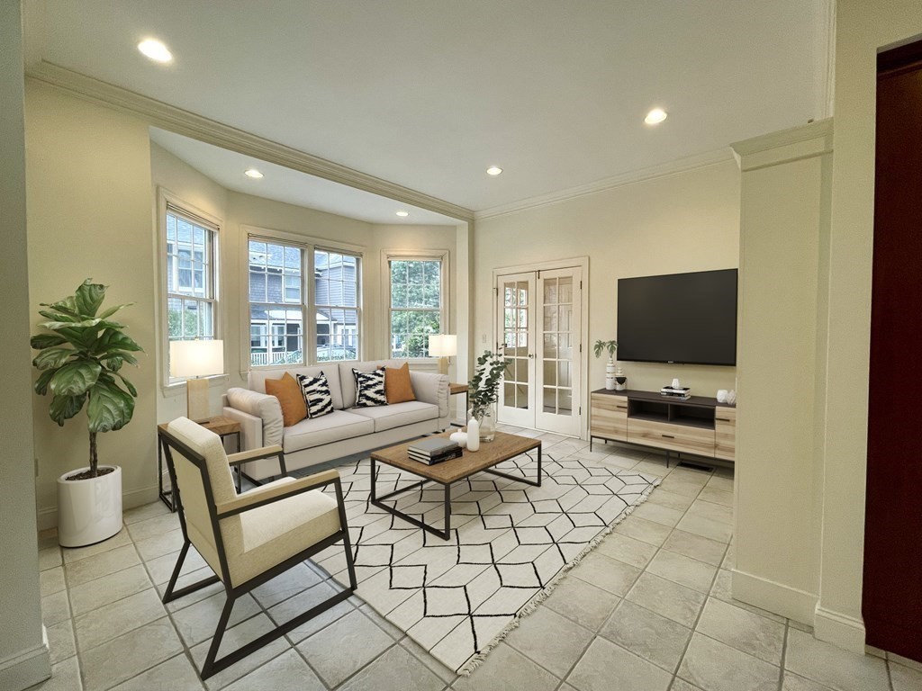 Living room with bay windows, a light sofa, geometric rug, and wall-mounted television.