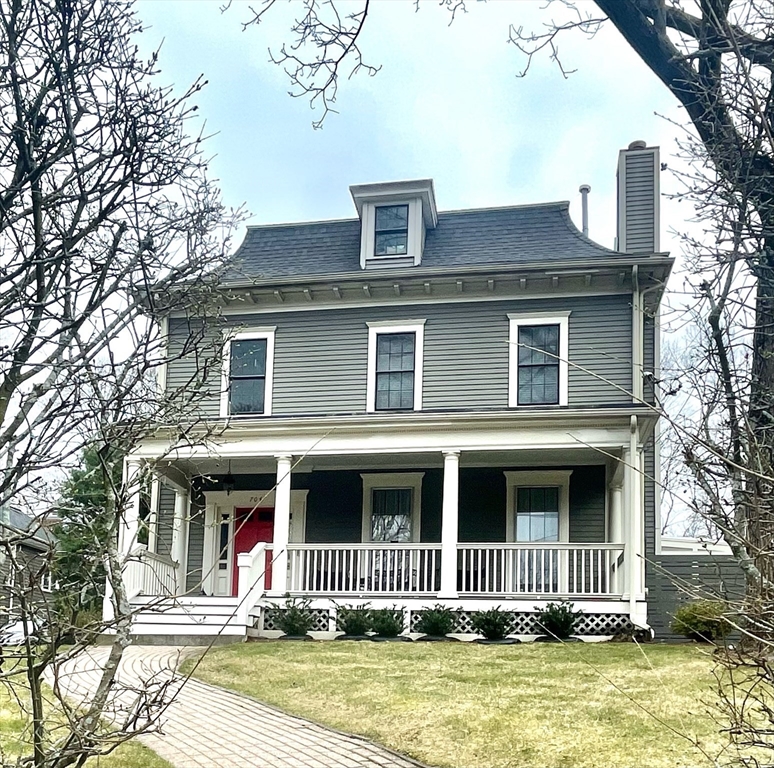 Gray two-story house with a red front door, white-trimmed porch, and roof dormer.