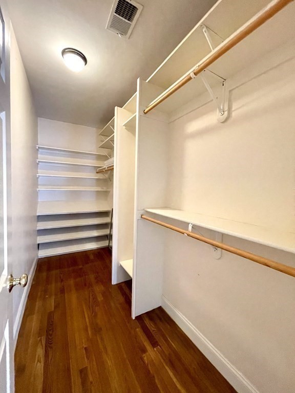 Walk-in closet with built-in shelving, hanging rods, and dark hardwood floors.