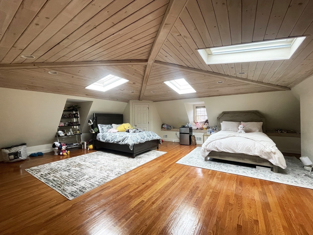 Attic bedroom with two beds, polished hardwood floors, a wood-paneled ceiling, and skylights.