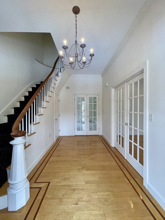 Entry hall with an inlaid hardwood floor, curved staircase, chandelier, and glass-paneled French doors.