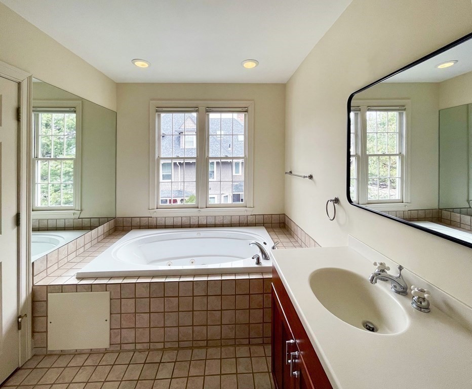 Bathroom with an inset jetted tub, tiled surround, and long vanity beneath a large mirror.