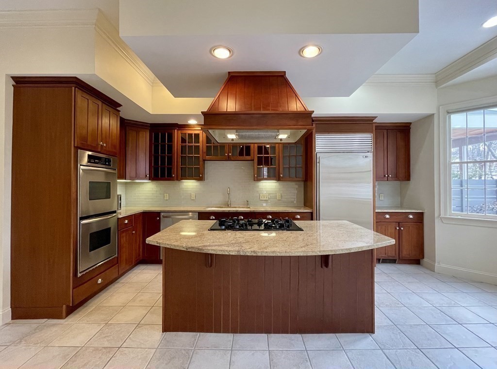 Kitchen with a granite island and cooktop, dark wood cabinets, and stainless steel appliances.