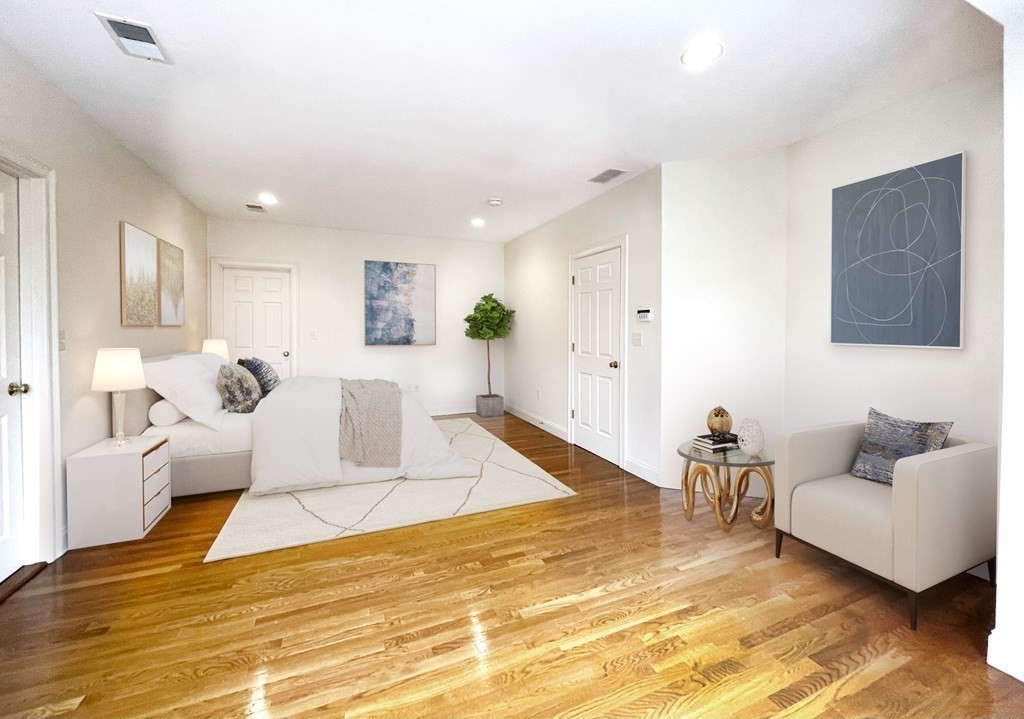 Staged bedroom with a white bed, polished hardwood floors, and a cream armchair.