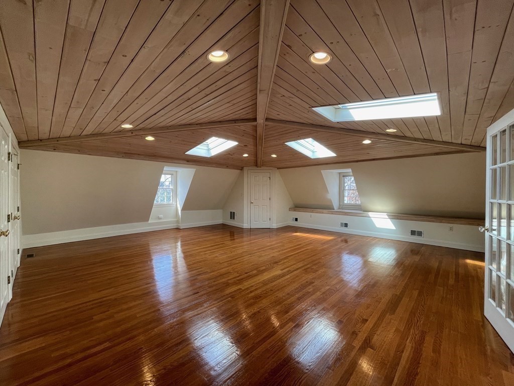 Vacant finished room with glossy hardwood floors and a vaulted wood ceiling with skylights.