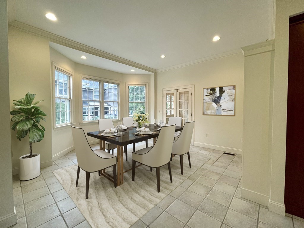 Staged dining room with a dark table, upholstered chairs, tiled floors, and a bright bay window.