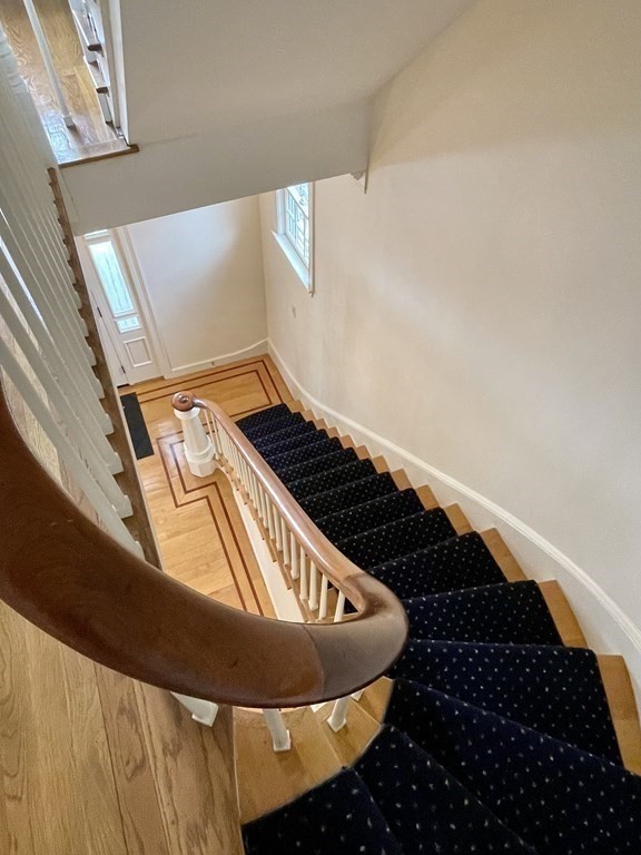 Curved staircase with a dark runner, polished wood railing, and hardwood flooring.
