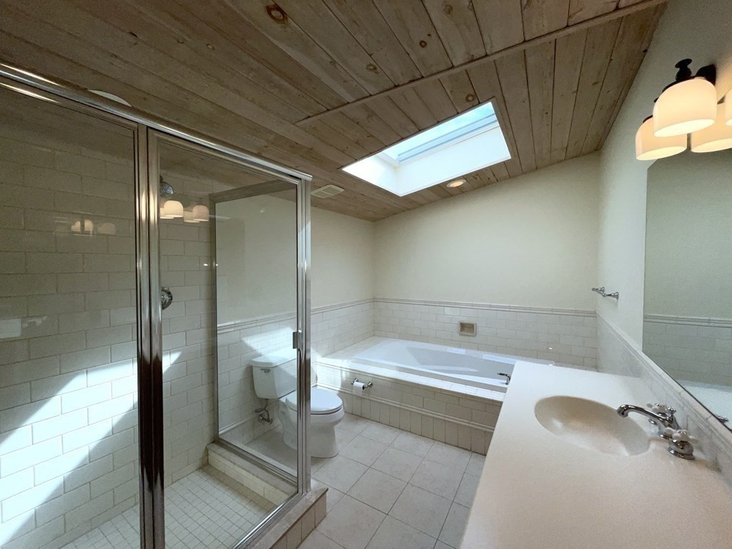 Bathroom with a glass shower, built-in tub, long vanity, and skylight beneath a wood-plank ceiling.