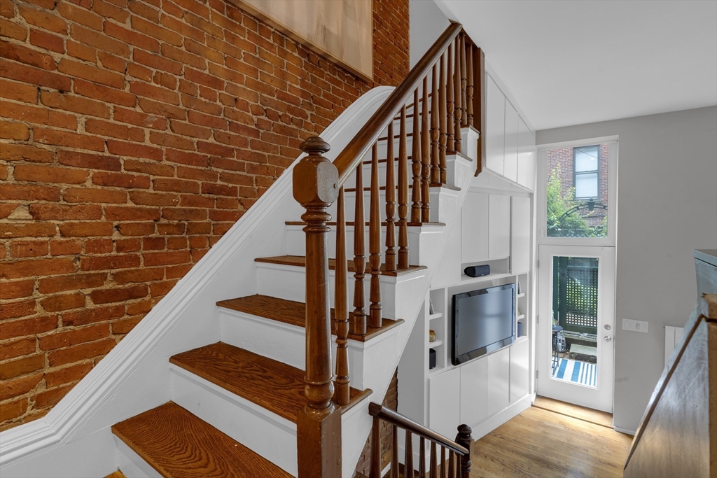 Staircase with dark wood treads and banister beside an exposed brick wall and built-in television shelving.