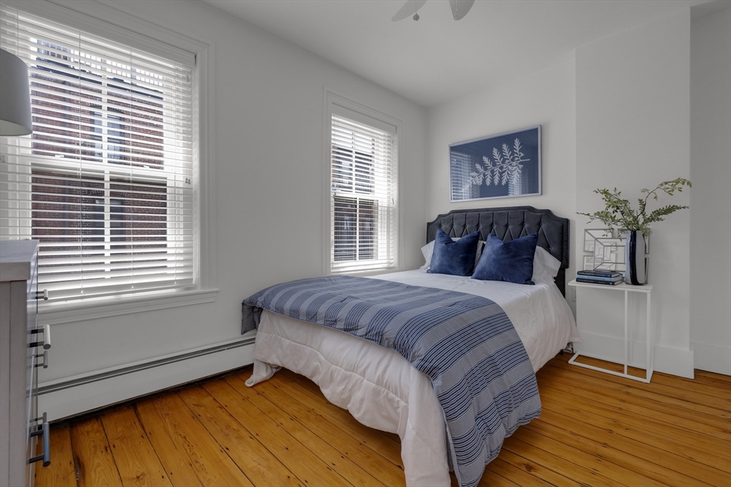 Bedroom with blue striped bedding, a dark tufted headboard, two bright windows, and hardwood floors.