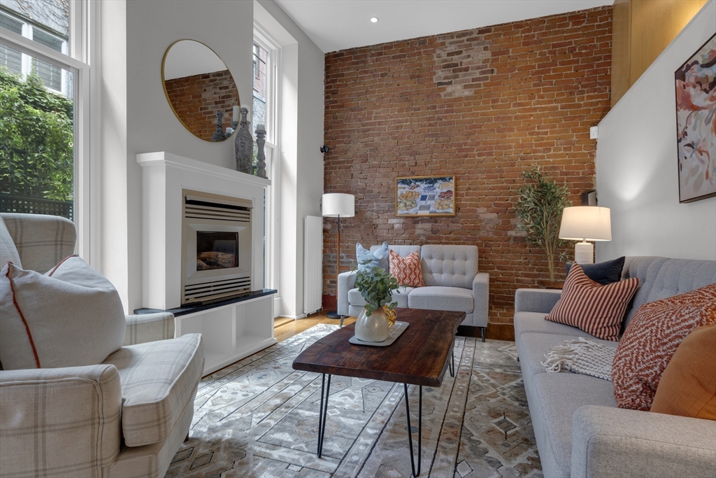 Living room with an exposed brick wall, white fireplace, and tall windows.