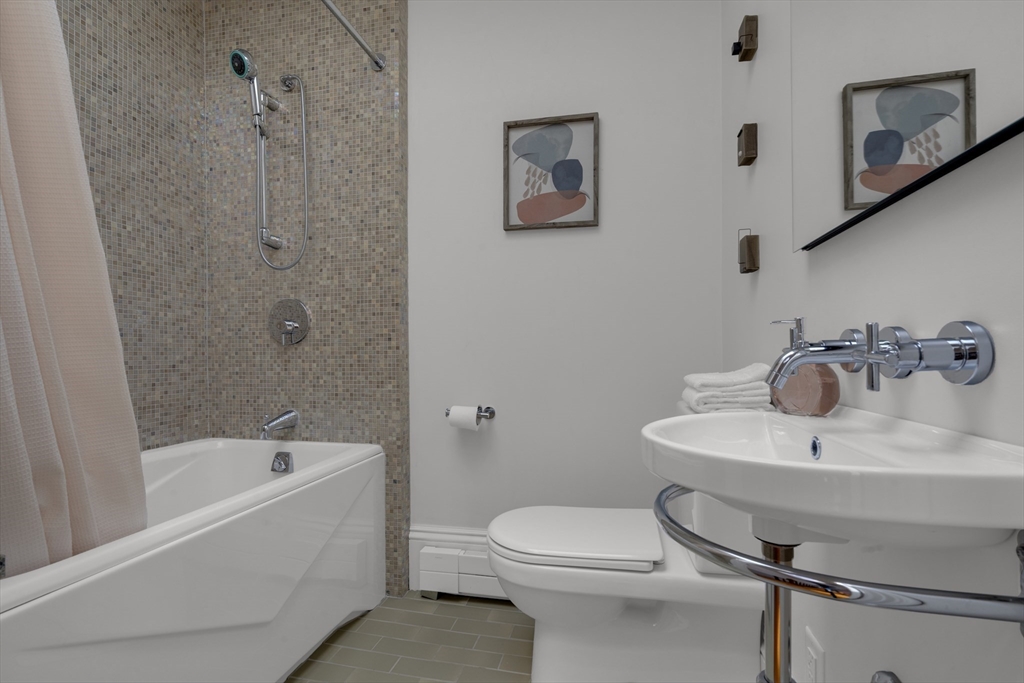 Bathroom with a mosaic-tile shower, white bathtub, toilet, and wall-mounted sink.