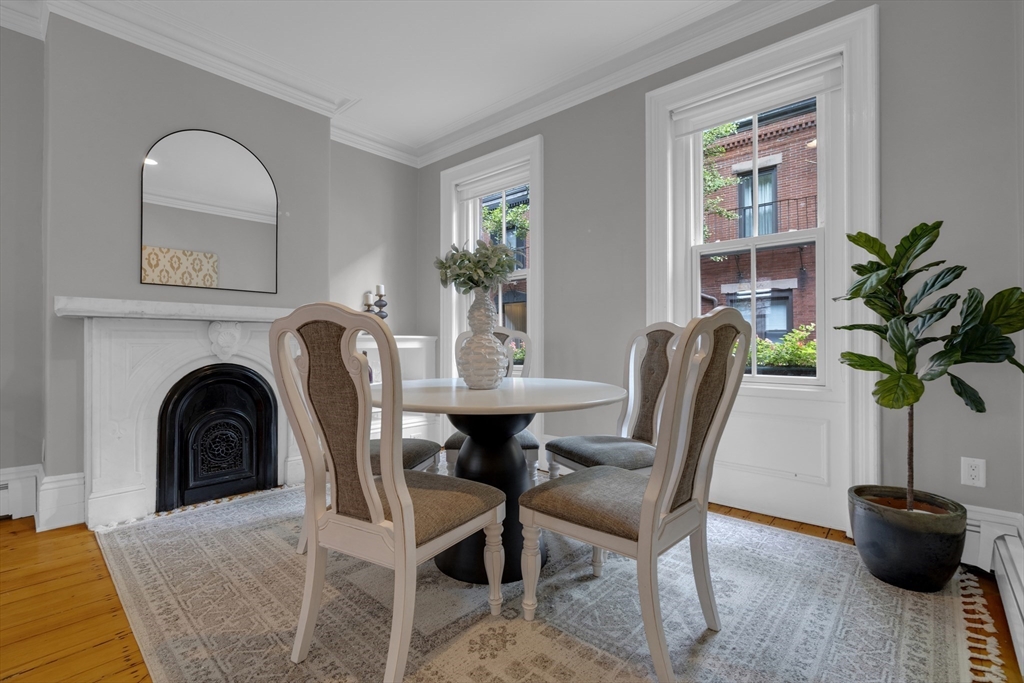 Dining room with a round table, white fireplace, tall windows, and hardwood floors.