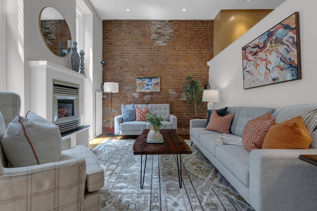 Living room with exposed brick wall, fireplace, gray seating, and a dark wood coffee table.