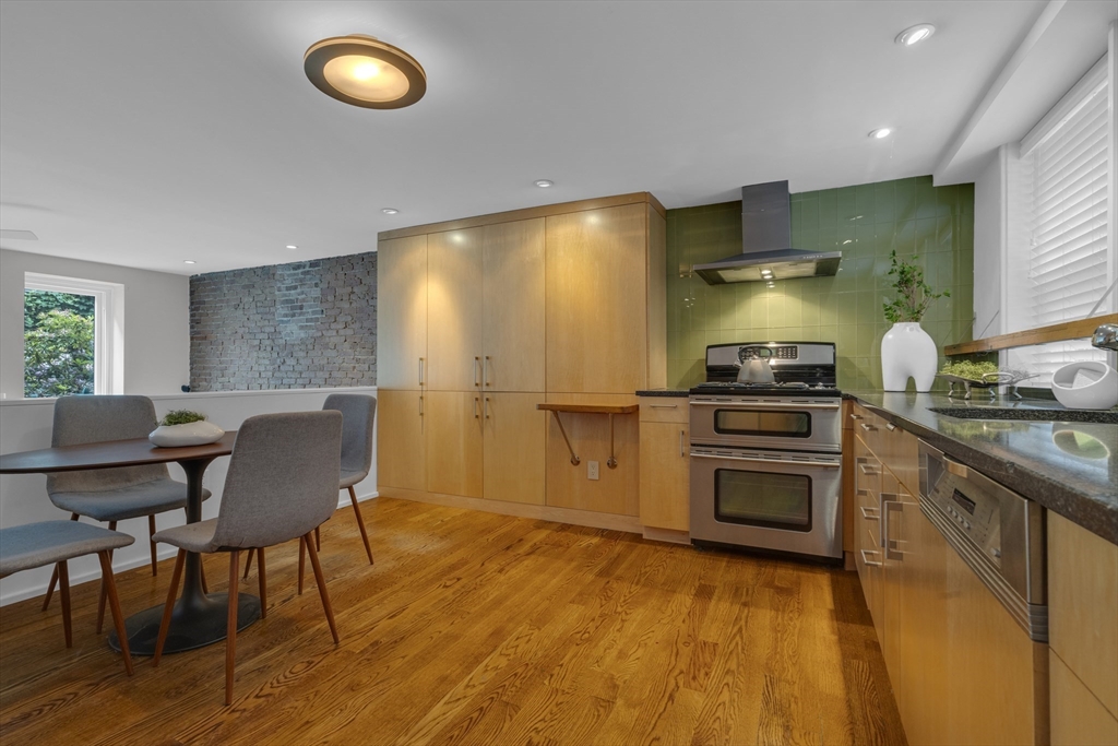 Kitchen with light wood cabinetry, green tile backsplash, stainless steel range, and adjoining dining area.