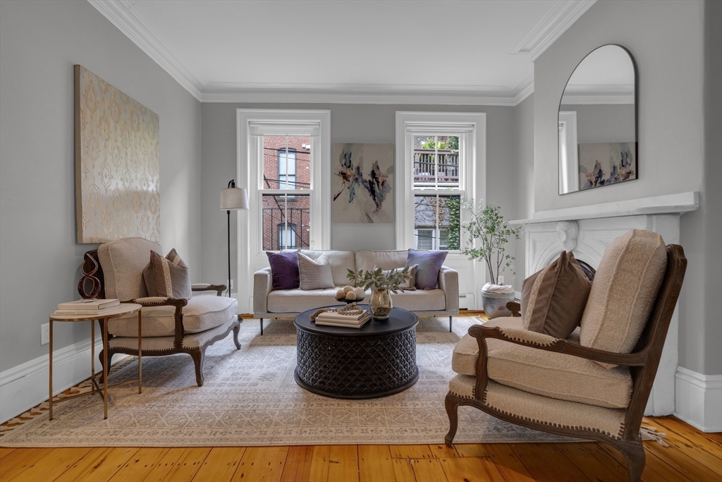 Living room with a white fireplace, tall windows, upholstered seating, and hardwood floors.
