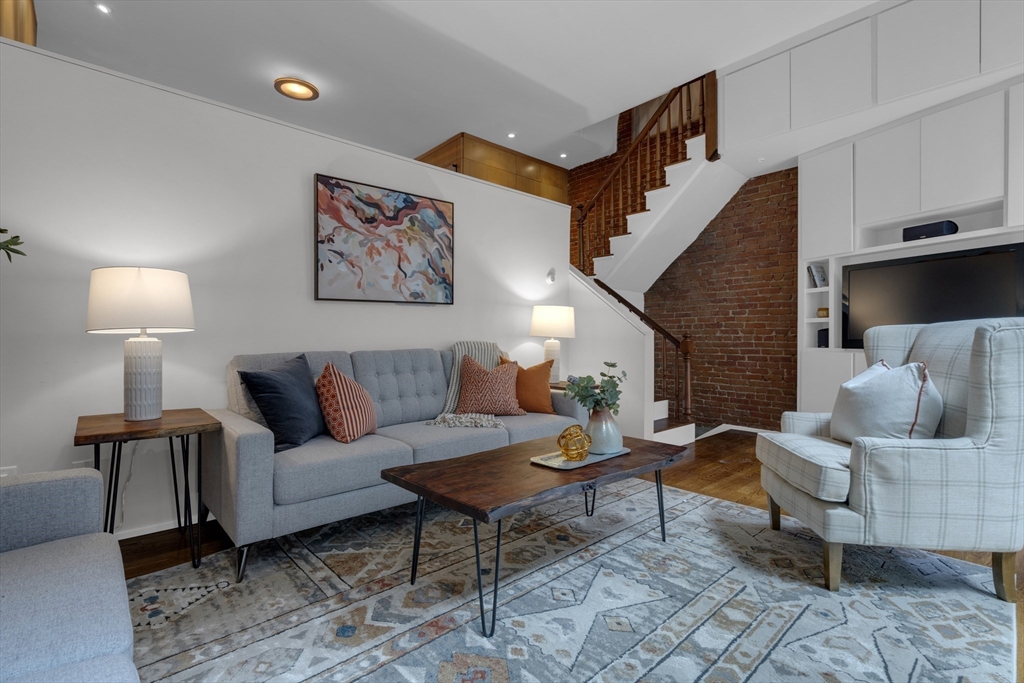 Living room with gray sofa, plaid armchair, built-in TV cabinetry, and exposed brick staircase.