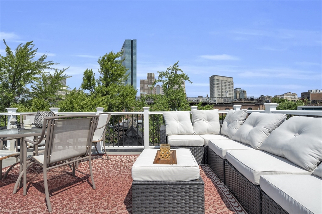 Rooftop terrace with white-cushioned sectional seating and dining set overlooking the Boston skyline.