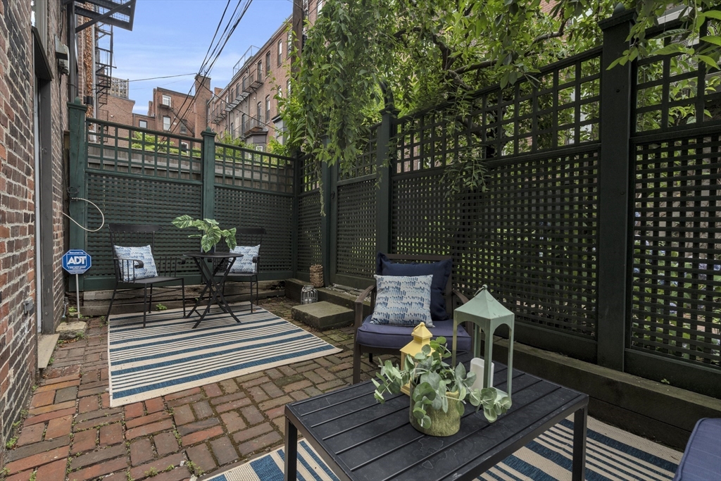 Brick patio courtyard with lattice fencing, outdoor seating, striped rugs, and potted plants.