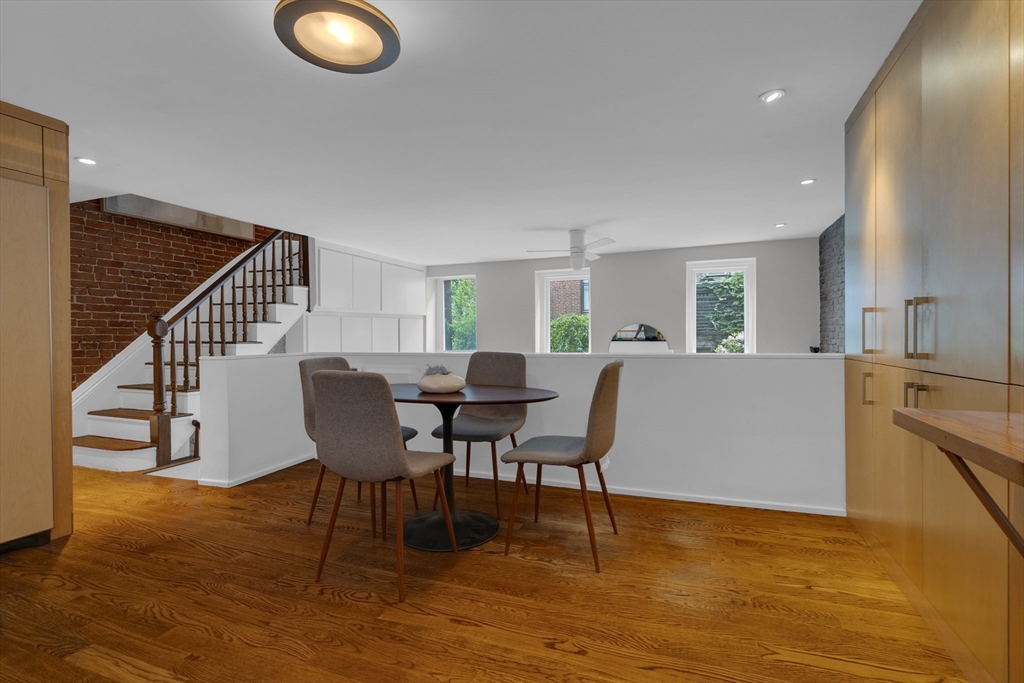 Dining area with a round table, hardwood floors, and a staircase against exposed brick.