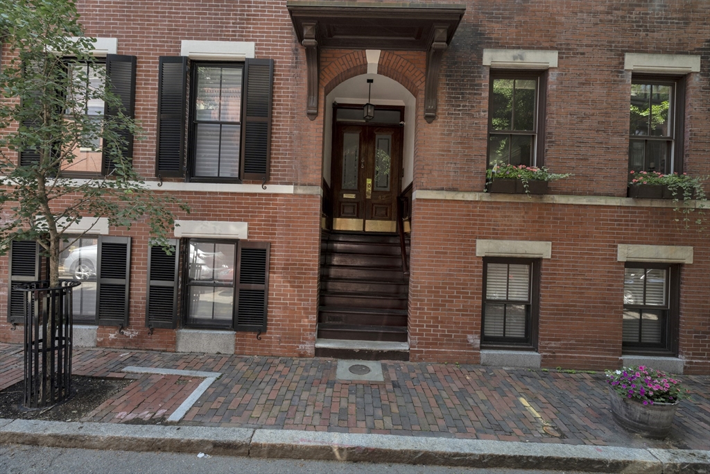 Red-brick building with a raised central entrance, black shutters, and window flower boxes.