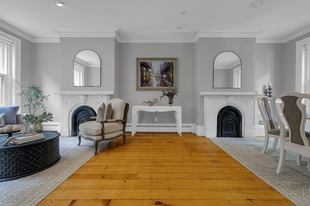 Formal living room with two white fireplaces, arched mirrors, and wide honey-colored wood floors.