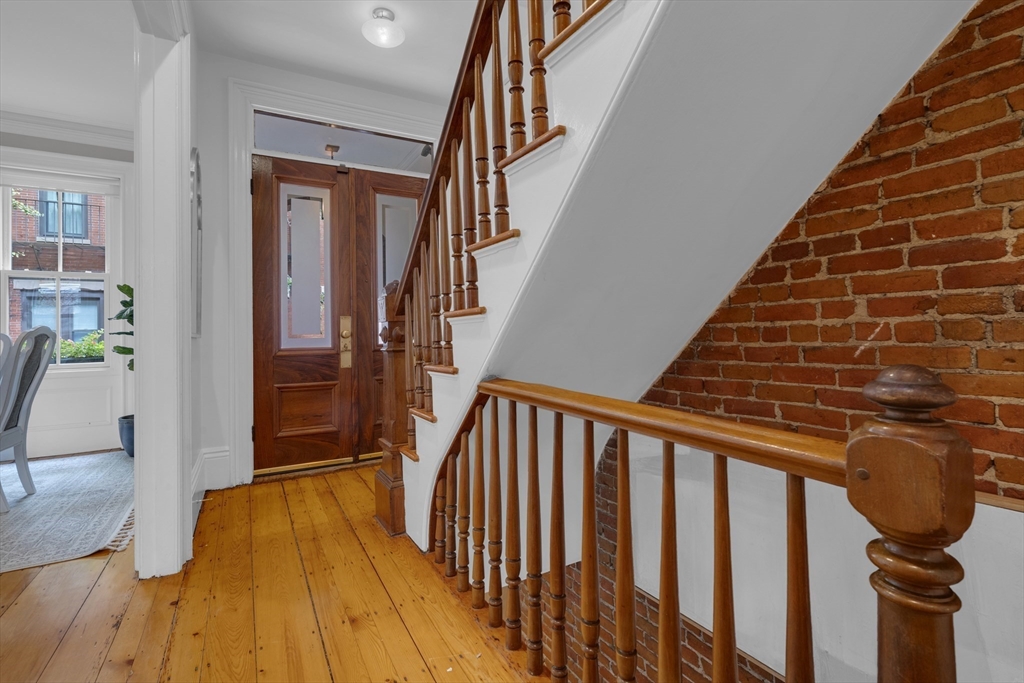 Entry hall with hardwood floors, a turned wood staircase, and an exposed brick wall.