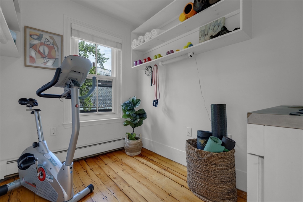 Home exercise room with a stationary bike, yoga equipment, open shelves, and warm wood floors.
