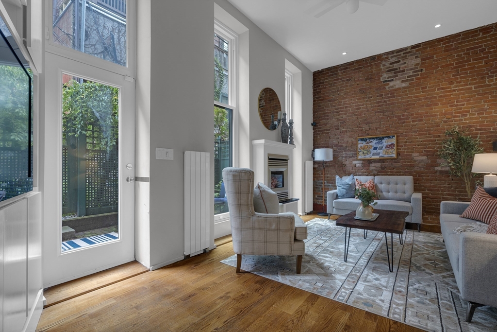 Living room with an exposed brick wall, fireplace, tall windows, and a glass door to the patio.