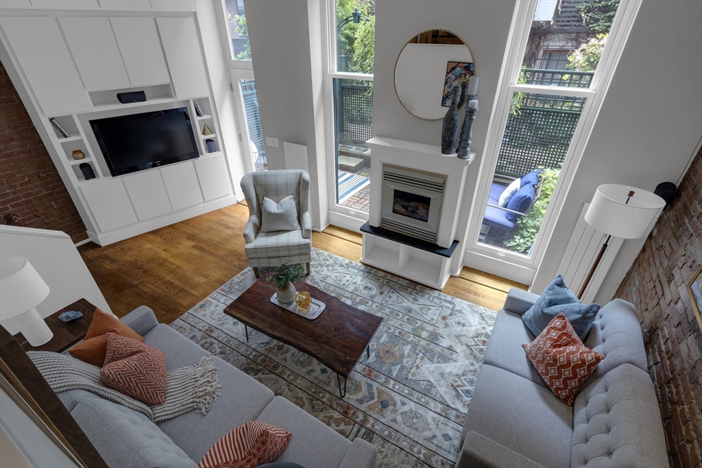 Living room with exposed brick, tall patio-facing windows, a fireplace, and gray sofas.