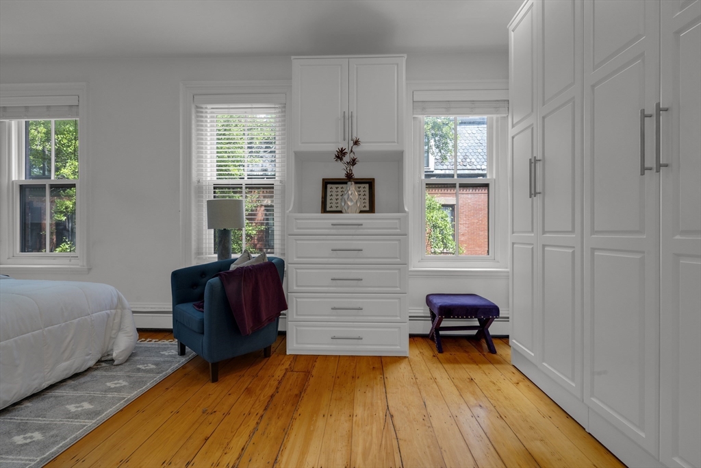 Bedroom with white built-in cabinetry, honey-toned hardwood floors, and a teal armchair.