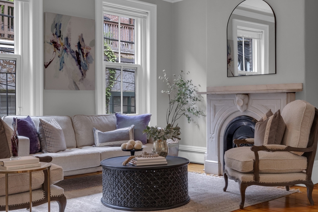 Living room with tall windows, a decorative fireplace, pale seating, and a round black coffee table.