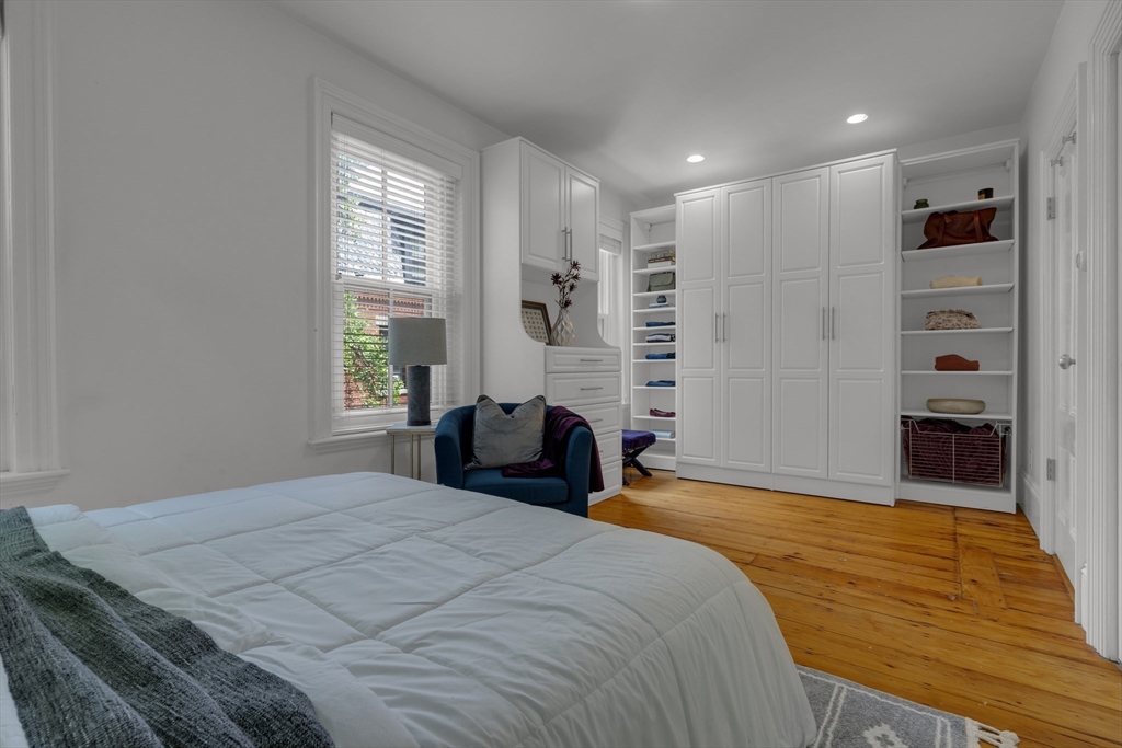 Bedroom with built-in white wardrobes, open shelving, a blue armchair, and hardwood floors.