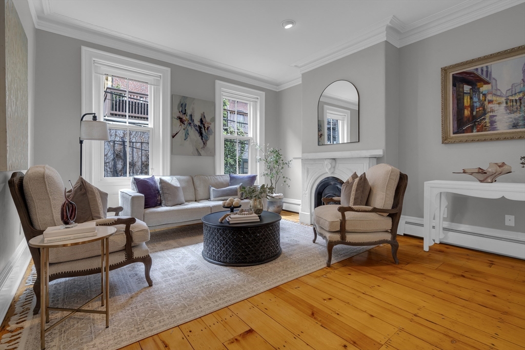 Living room with a white fireplace, gray sofa, upholstered armchairs, and warm wood floors.