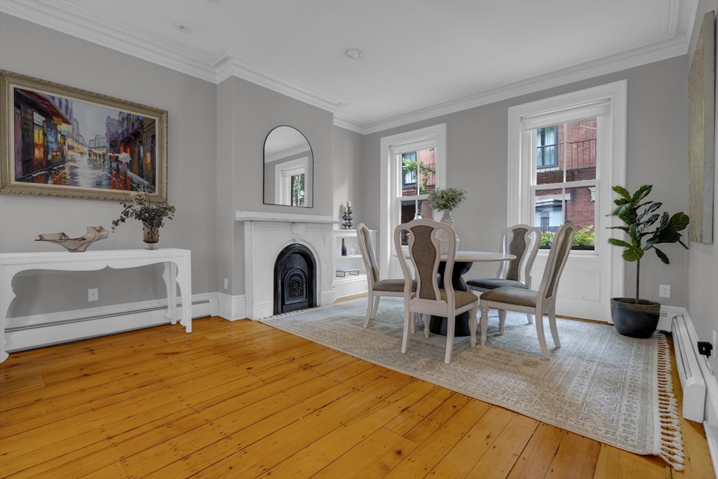 Dining room with a white fireplace, round table, tall windows, and honey-colored wood floors.